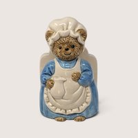 A vintage ceramic Otagiri napkin holder shaped like an anthropomorphic brown bear wearing a blue dress, white apron, and bonnet against a neutral background.