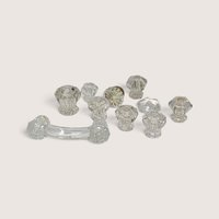 A collection of 10 assorted vintage clear glass cabinet knobs and one curved drawer pull laid out on a neutral background.