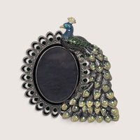 An ornate vintage metal photo frame shaped like a peacock with blue and green enamel detailing and sparkling rhinestone crystal accents surrounding an oval picture opening.