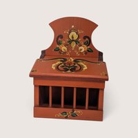A vintage reddish-brown wooden onion box featuring traditional hand-painted floral folk art designs, a slatted front grill, a hinged lid, and a wall-mounting hole on the upper back panel against a neutral background.