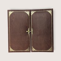 A vintage brown tri-fold photo album with gold filigree corner accents and a central gold-tone metal latch closure resting against a neutral background.