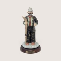 A vintage Flambro Emmett Kelly Jr. porcelain skier figurine featuring a clown holding skis on a wooden base.