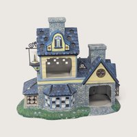 A vintage PartyLite Old World Village ceramic candle shoppe building featuring blue shingle roofs, yellow siding, stone accents, and a hanging lantern.