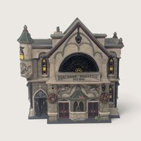 A vintage Department 56 Theater of the Macabre Halloween village building featuring gray stone details, skull carvings, double doors, and glowing windows.