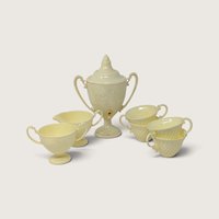 A vintage yellow plastic child serving set including a tall urn, creamer, sugar, and four cups on a neutral background.