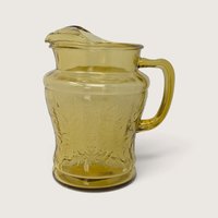 A vintage Federal Glass amber yellow depression glass pitcher featuring the Madrid scroll pattern on a neutral background.