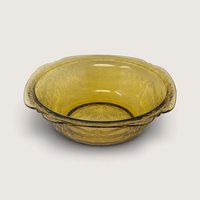 A vintage yellow glass serving bowl featuring an embossed scroll pattern on a neutral background.