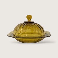 A vintage yellow glass covered butter dish featuring an embossed scroll pattern and domed lid on a neutral background.