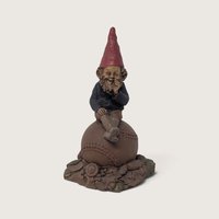 A vintage signed Tom Clark Homer gnome figurine sitting atop a leather baseball on a textured leaf and acorn base against a neutral background.