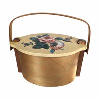 A vintage wooden woven basket with a hinged lid featuring a hand-painted floral design of a pink rose and blue flowers, with a stationary arched wood handle.