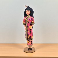 A vertical view of a 1997 Hallmark Keepsake ornament featuring Barbie as part of the Dolls of the World collection. She is wearing a traditional pink floral-patterned kimono with gold trim, her long black hair styled in a high ponytail with a decorative pink flower accessory.