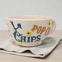 Large ceramic mug featuring a handpainted design with the Pop Chips logo in bold red and blue lettering. The piece has a wide, sturdy handle and a glossy cream-colored glaze.