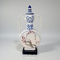 A large, circular porcelain moon flask with a slender neck and two small handles. The face features a detailed blue and white transfer of a blooming lotus and rose, set against a stark white glaze.