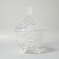 A tall, clear crystal candy dish with a matching lid. The exterior features a bold, swirling serpentine texture that winds around the body and finial, creating a fluid, rippled glass effect.