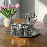 Classic pewter service set including a rectangular handled tray, a slender pitcher, and six small tumblers. Smooth matte grey finish with traditional German relief crests and ornamental detailing on the vessel bodies.
