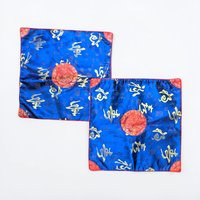 Two square satin pillow covers in a deep cobalt blue with metallic gold calligraphic characters. A central red circular medallion with gold embroidery anchors the design, and red brocade corners finish the edges.
