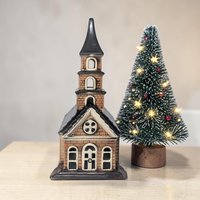 A ceramic village church with a tiered steeple and brick-patterned walls in tan and deep brown. The structure features cream-colored arched windows and a circular rose window detail. Smooth, glazed finish with a dark, flared base.