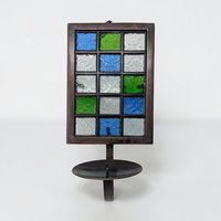 A tall black metal wall sconce featuring a grid of twelve square glass inserts in shades of forest green, cerulean blue, and opaque white. The rectangular frame has a single candle cup at the base and a circular hanging loop.