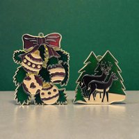 Set of two ornaments featuring a large textured gold-tone metal bow and a separate resin scene of a reindeer standing between snow-covered evergreen trees.