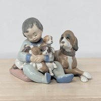 A pale blue and white glazed porcelain figurine featuring a young girl in a long dress kneeling beside a small puppy. The girl wears a wide-brimmed sun hat, and the piece is finished in the signature Lladro pastel color palette.