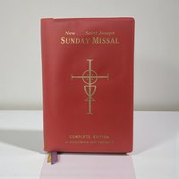 A thick, pocket-sized softcover book with a flexible white cover featuring a golden religious emblem. The spine is substantial, and the thin cream-colored pages show a slight natural rippling from age.