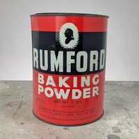 A large cylindrical metal tin with a bold red and black label. White block lettering reads RUMFORD BAKING POWDER. A white oval at the top contains a black silhouette of a man's profile framed by a laurel wreath.