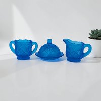 A three-piece miniature toy glassware set in vibrant sky blue. Includes a tiny lidded butter dish, a small creamer, and a matching sugar bowl, all featuring a repeating thumbprint indentation pattern.