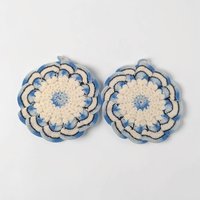Two circular hand-crocheted pot holders in a crisp blue and white color scheme. One features a white center with a blue border, the other a blue center with a white border. Intricate radiating stitch patterns with hanging loops.