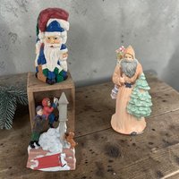 Three festive Santa figurines including a seated Santa writing a letter, a vertical stack of Santas, and a classic ceramic Santa holding a miniature tree.