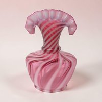Cranberry pink glass vase with diagonal opaque white opalescent swirls. The silhouette features a bulbous body, narrow neck, and a wide, ruffled fan-shaped rim. The texture appears smooth and glossy with a delicate ribbed pattern.