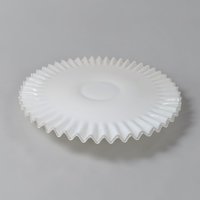 Opaque white milk glass plate with a smooth center and wide, deeply ruffled border edged in a thin ribbon of clear glass. The silhouette is low and circular with a repetitive, undulating texture along the perimeter.