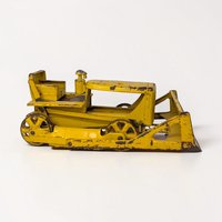 A heavy-duty yellow pressed steel bulldozer with a large front blade and visible surface oxidation. The silhouette is boxy and industrial, featuring a textured open cab and thick black rubber or plastic tracks.