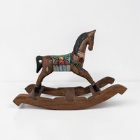 A dark wood rocking horse with a hand-carved texture. The horse features a black mane and tail, painted with a colorful saddle in teal, red, and yellow. It is mounted on a sturdy curved wooden rocker base with visible grain.