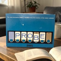 A blue rectangular game box sitting on a wooden table. The word "PROBE" is displayed across the bottom in stylized white cards with blue lettering. A small white scuff is visible on the center of the blue background.