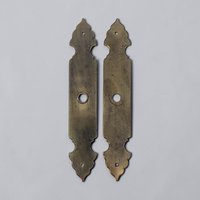 A pair of long brass escutcheon plates with a rectangular center and ornate scalloped ends. The metal has a heavily aged, dark gold patina with central circular cutouts and smaller mounting holes at each tip.