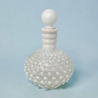 A vintage Fenton white milk glass cologne bottle with a spherical hobnail texture. The bottle features a ribbed neck and a matching smooth round glass stopper on a bulbous silhouette against a light blue background.
