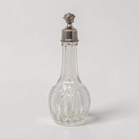 A 5-inch clear glass bottle with a teardrop silhouette and a ribbed faceted texture. It features a long slender neck topped with a decorative silver-tone metal cap featuring a rose floral finial.