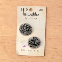 Two circular silver tone buttons on a white card. The buttons feature an intricate openwork filigree design with swirling patterns and beaded textures. They have a high-shine metallic finish and a domed silhouette.