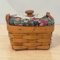 A small square woven maple wood basket with a single swinging handle. The weave features a single green horizontal accent strip near the top rim. The base is solid wood and the interior is unlined.
