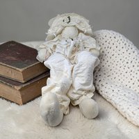 A large cream-colored handmade plush bunny with exceptionally long, slender ears and limbs. The bunny features a hand-stitched face and wears a vintage-style fabric outfit with a lace collar. It is shown in a seated pose with a weighted base.