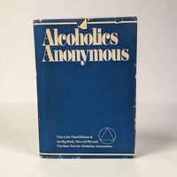 A navy blue dust jacket with bold, cream-colored serif typography reading Alcoholics Anonymous. The jacket features a circular emblem with a triangle inside at the bottom right. Visible wear and small tears are present along the top edge of the spine.
