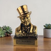 A metallic gold and black ceramic decanter shaped like a man's bust wearing a top hat and bow tie.