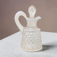 A 4-inch miniature Fenton art glass cruet in white opalescent hobnail. The clear glass base transitions to milky white studs on a flared silhouette, featuring an elegant pouring spout, a curved handle, and a matching hobnail stopper.