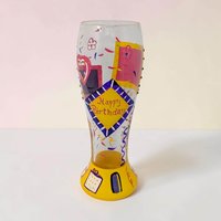 Tall clear glass pilsner with hand-painted yellow, pink, and purple geometric shapes, scattered confetti, and a yellow diamond reading Happy Birthday in red script atop a vibrant yellow base.