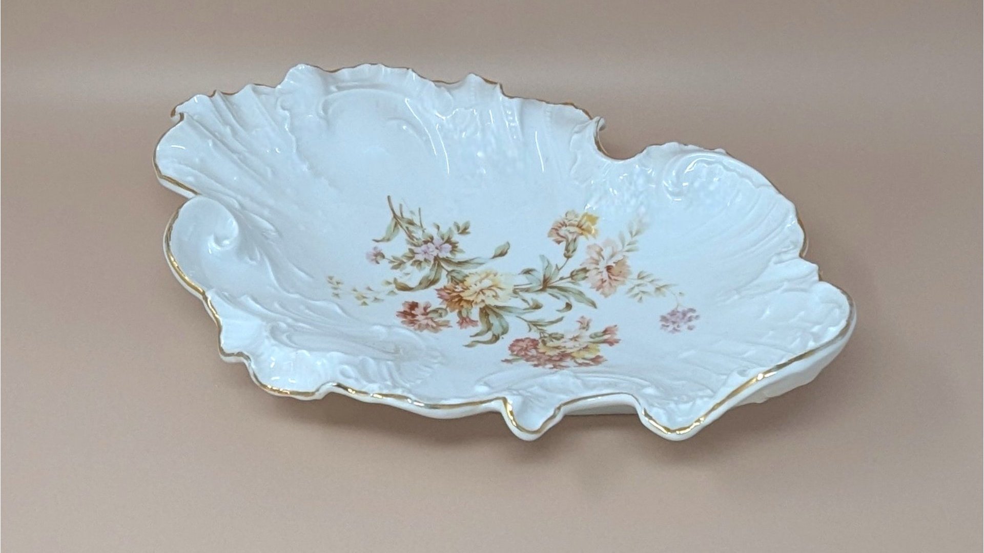 Large, ornate Carl Tielsch porcelain bowl with a highly ruffled, scalloped edge and gold gilt trim. Features embossed scrollwork and a central transfer of autumnal wildflowers in peach, pink, and yellow.