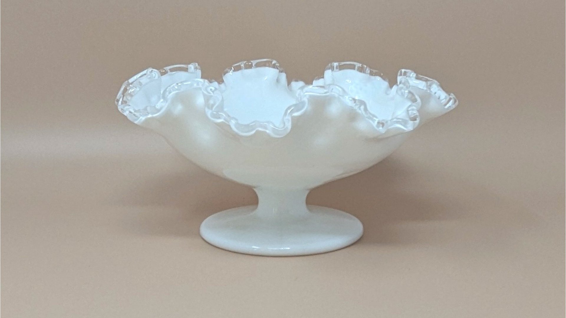 Fenton milk glass compote with a pedestal base and wide, ruffled rim. Features an opaque white body with a clear glass "Silver Crest" edge, set against a neutral background.
