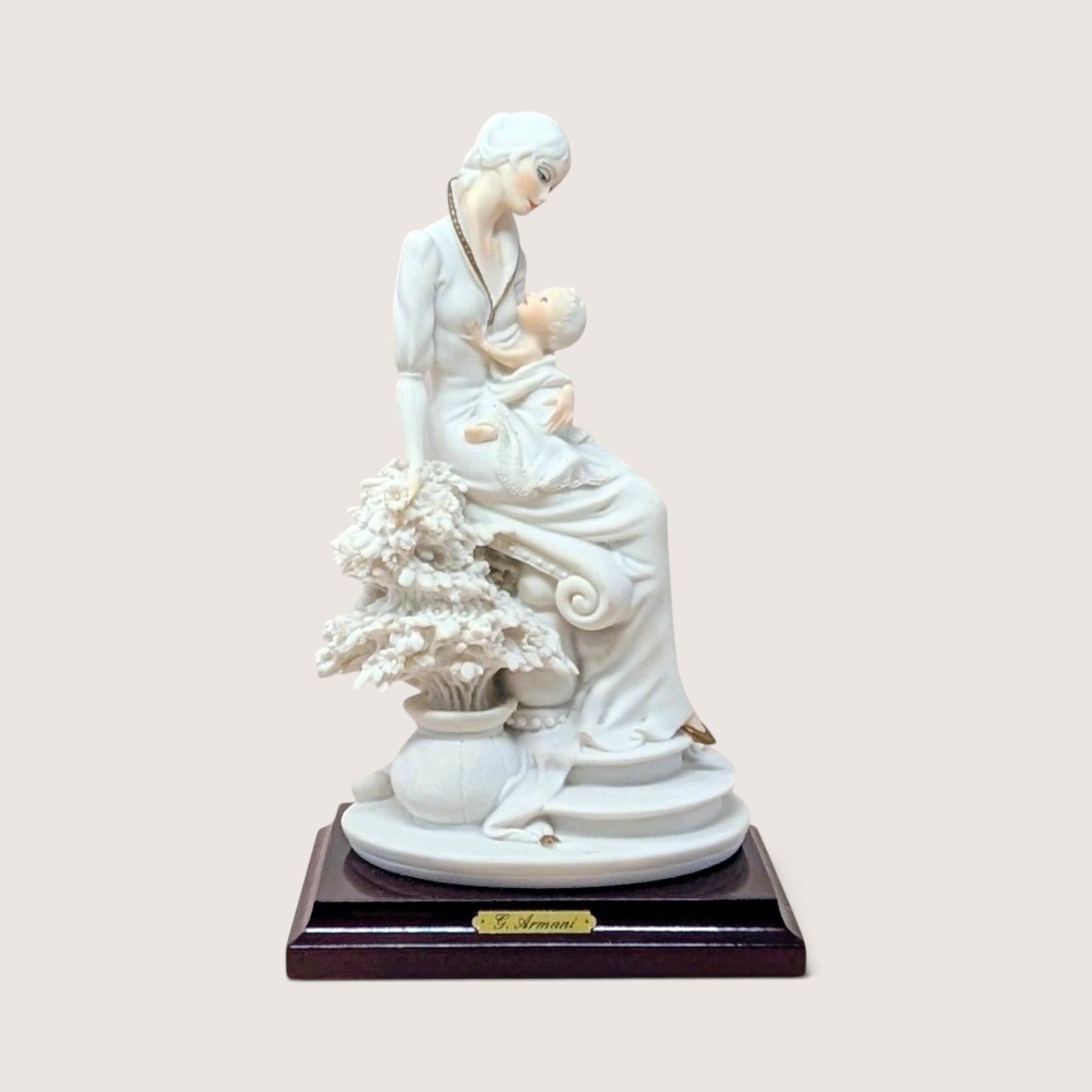 Vintage 1992 Giuseppe Armani porcelain figurine of a mother and child seated next to a floral sculpture on a wooden base.