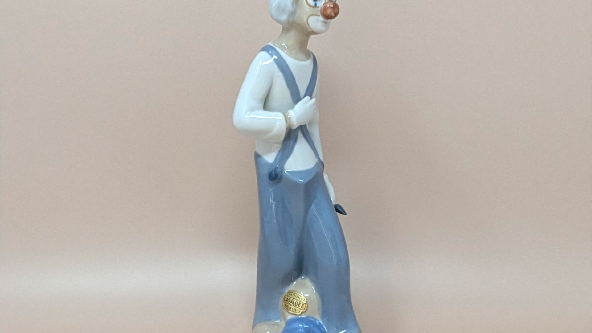 Slender Cascades Spanish porcelain figurine of a melancholic clown. Features a muted palette of slate grey and dusty blue with a high-gloss finish. Hand-painted details on the face and ruffles, 9.5 inches tall.