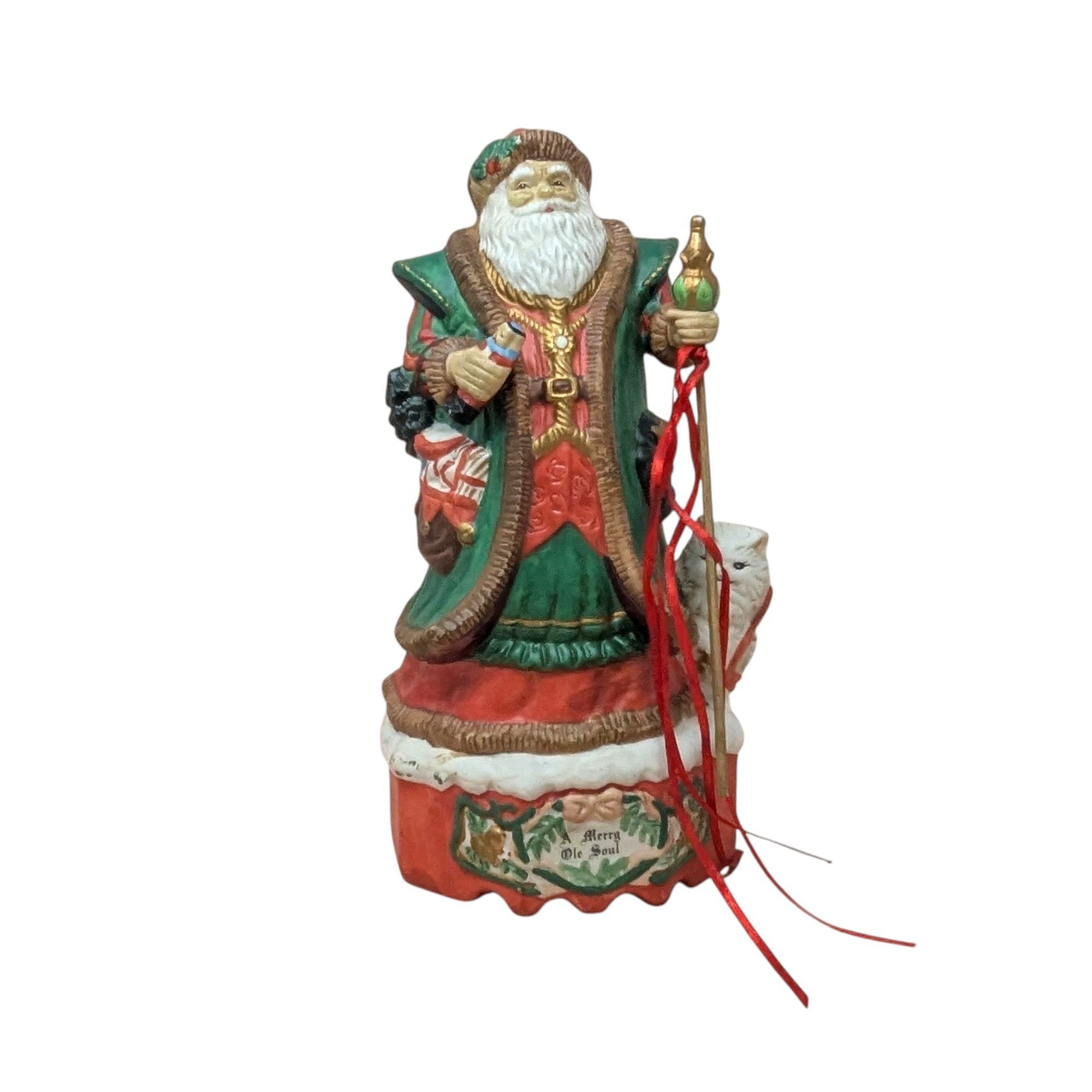 A hand-painted ceramic Old World Santa figurine on a musical base. He wears a green and red robe, holding a staff with red ribbons and a nutcracker. A white bear cub sits at his foot. The red base reads "Merry Ole Soul." The style is glossy and traditional against a plain beige background.