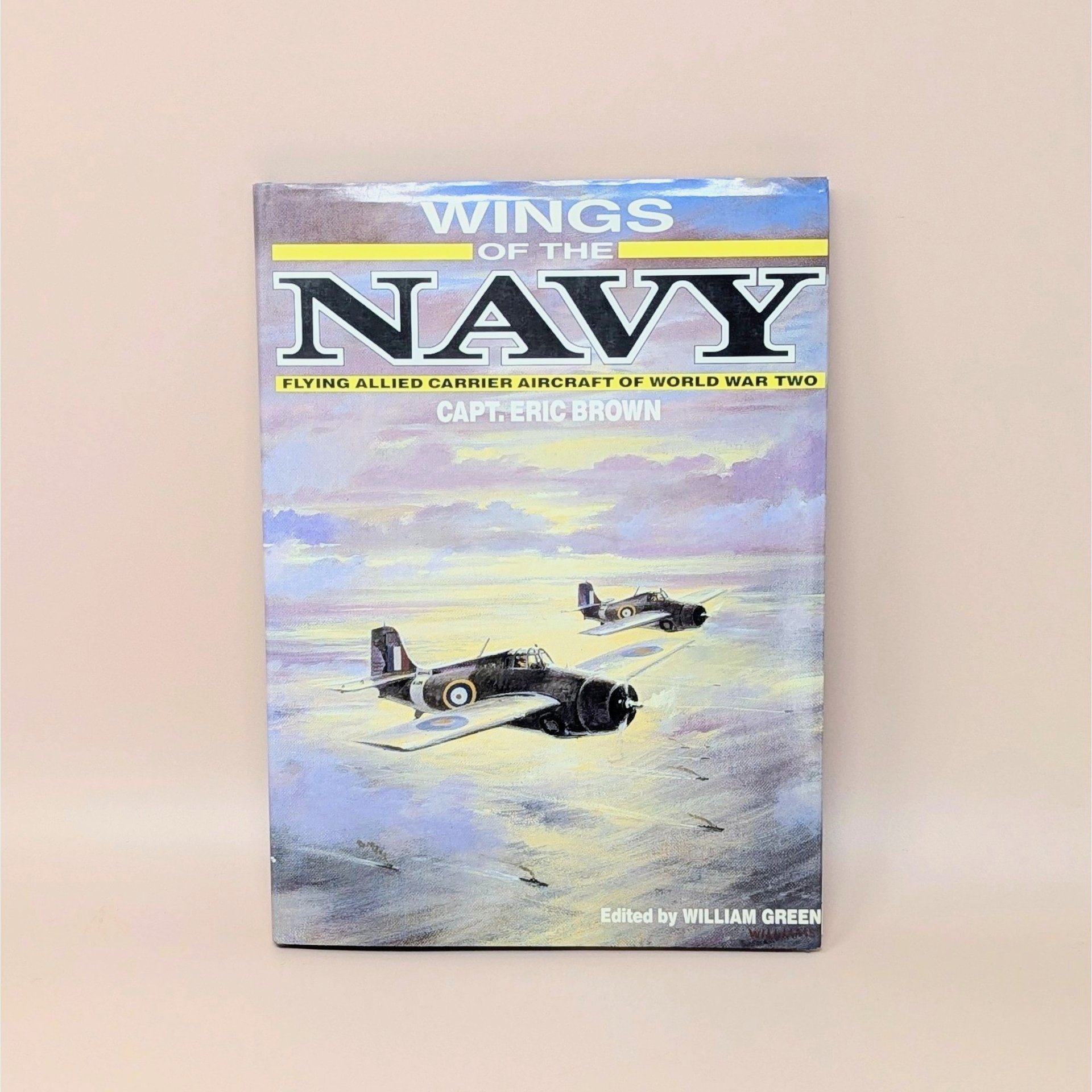 Hardcover book titled "Wings of the Navy" by Capt. Eric Brown. Dust jacket features a painting of two Allied fighter planes flying over a sunset-lit sea. 1987 edition.